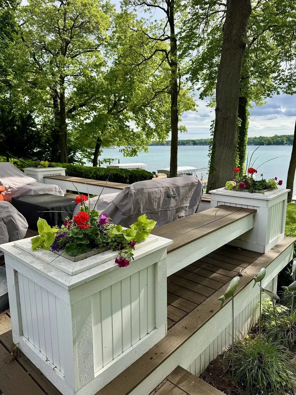 White planters with red geraniums on a lakefront deck