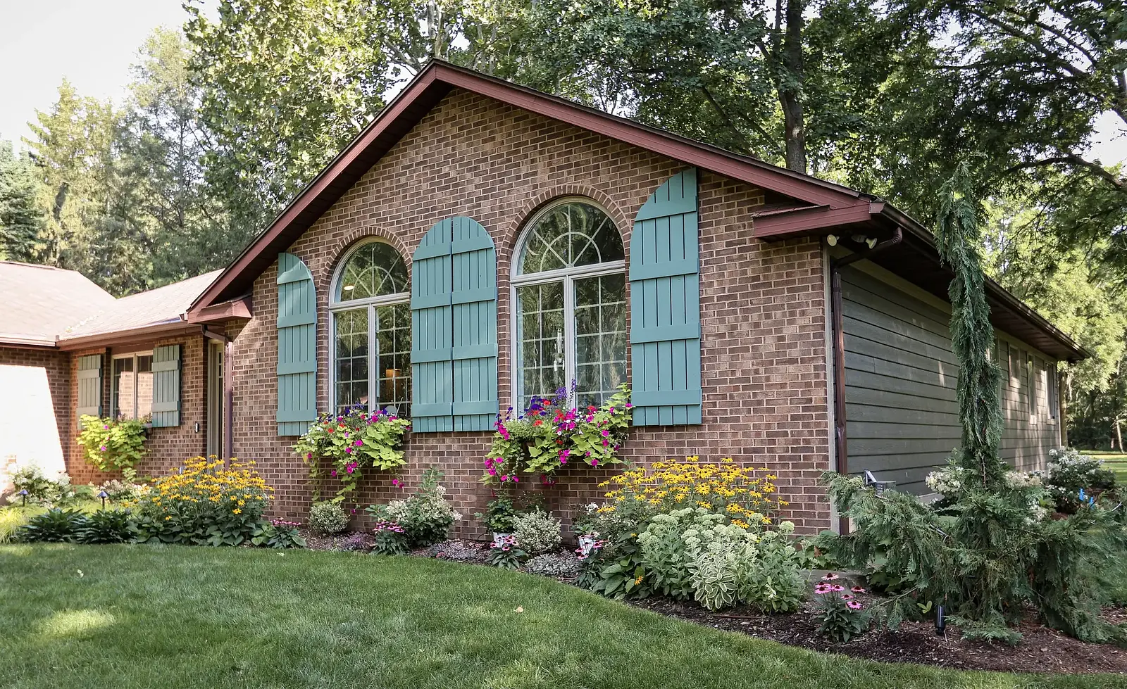 A brick house with blue shutters and foundation plantings of shrubs and perennials