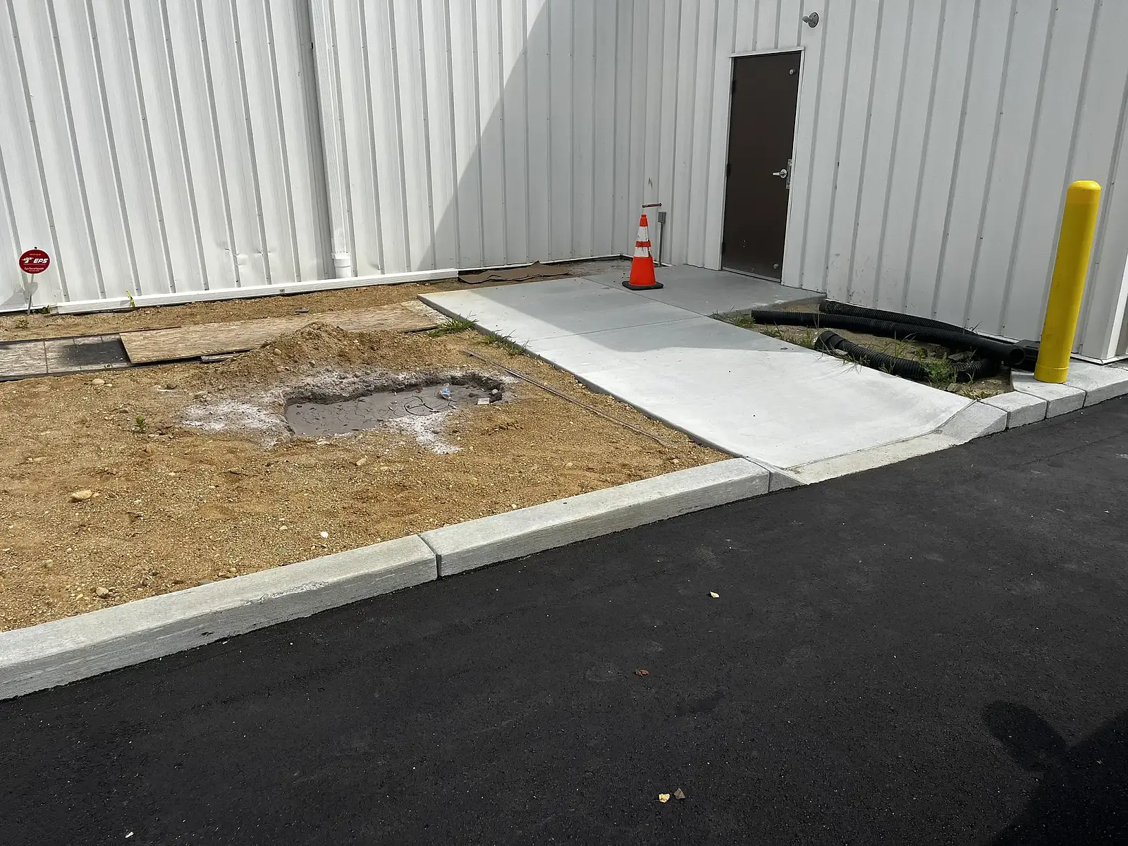 Bare ground beside a commercial building's side entrance before planting