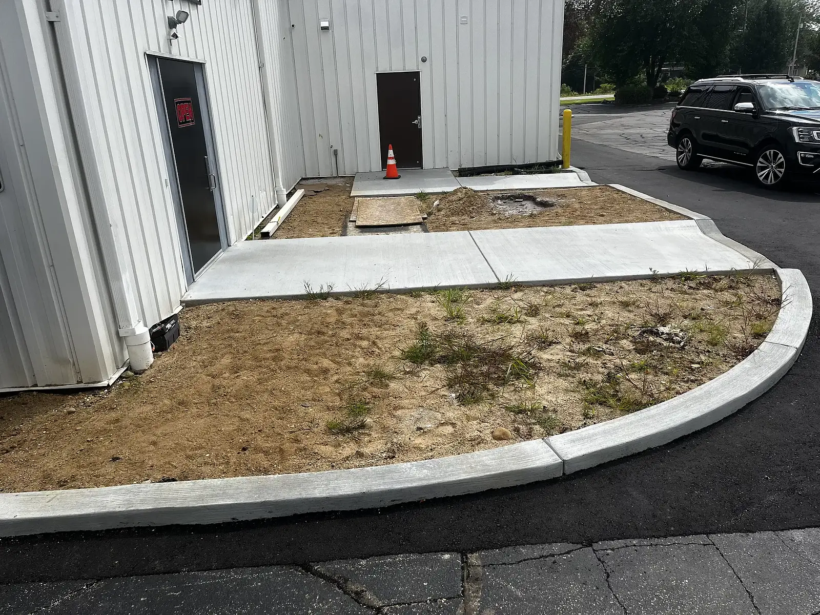 Bare, weedy ground at the corner of a commercial building before planting